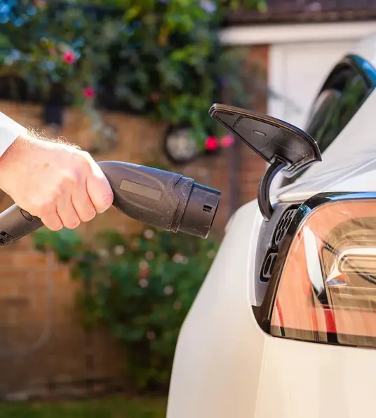 a person holding a power cord to a car